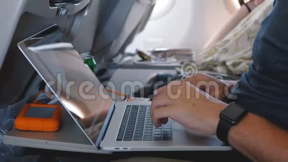 特写男性手与智能手表使用笔记本电脑在舒适的飞机商务旅行飞行在线工作视频的预览图