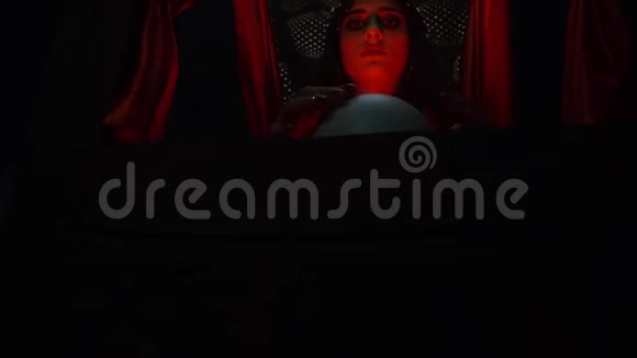 年轻女子召唤水晶球坐在红色灯光下算命先生视频的预览图