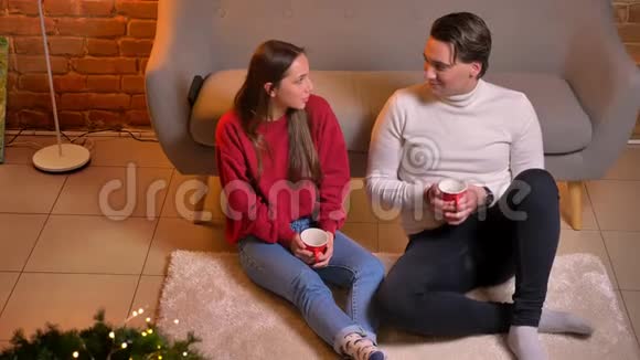 从上往下看快乐的白种人朋友坐在地毯上喝茶在圣诞节的家庭氛围中交流视频的预览图