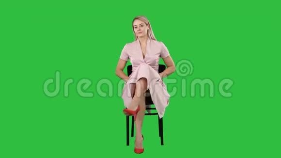 美丽的年轻女子女孩金发模特坐在椅子上看着绿屏上的镜头视频的预览图