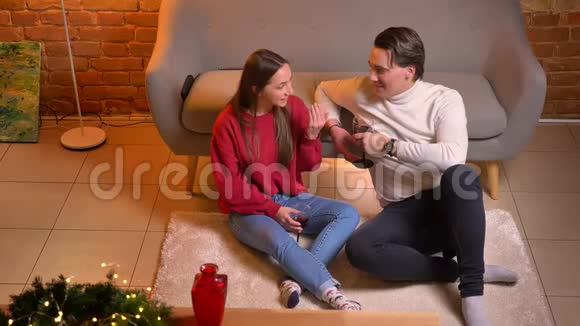 在舒适的家庭圣诞气氛中近距离从上往下看年轻的白种人朋友坐在地毯上喝酒视频的预览图