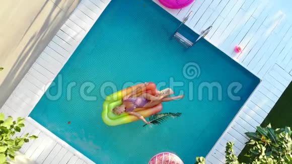 年轻女性沐浴在阳光下在空气床垫上的游泳池游泳俯视图视频的预览图