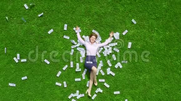 年轻漂亮而成功的女商人躺在一片绿草丛生的草坪上草坪上到处都是钱视频的预览图