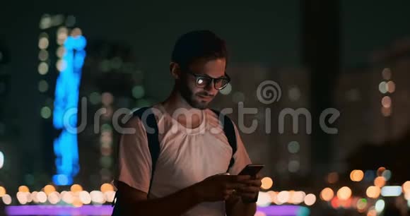 一个晚上戴眼镜的年轻人看着智能手机的屏幕视频的预览图