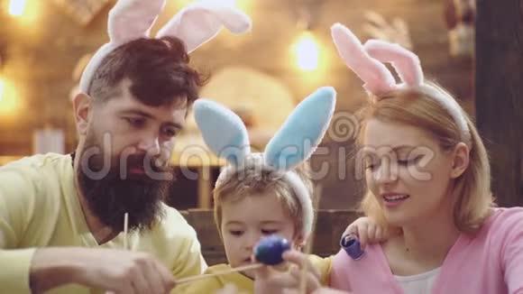 正在画复活节彩蛋的幸福家庭的特写可爱的小男孩戴着兔子耳朵母亲父亲和视频的预览图