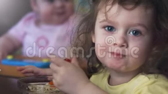 快乐的小女孩吃着粥吃着早餐坐在桌子上小妹妹在后台看着她视频的预览图