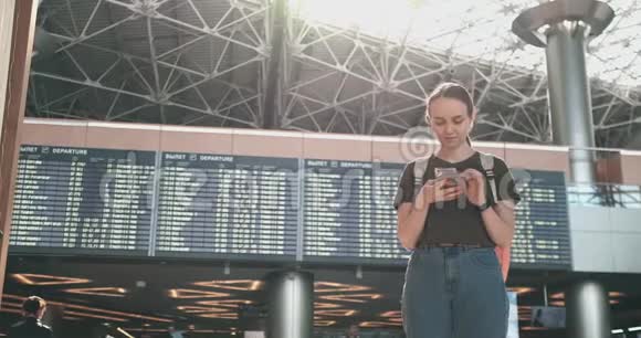 一位年轻女子在机场拿着一部智能手机在记分牌附近出发视频的预览图