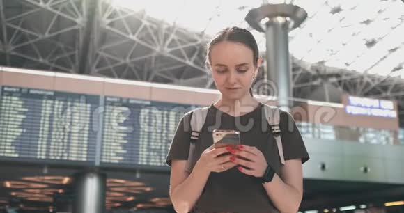 一位年轻女子在机场拿着一部智能手机在记分牌附近出发视频的预览图