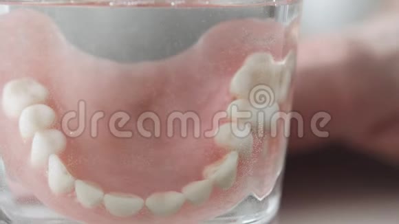 可移动的下颚玻璃特写一个人手把假牙放进一杯溶液里牙科护理慢动作4K视频的预览图