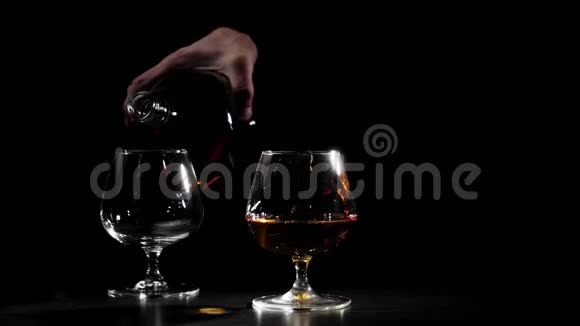 豪华白兰地穿着黑色衬衫的人从一个圆形的瓶子里把干邑倒入背景中的玻璃杯里白兰地白兰地嗅探器视频的预览图