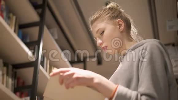 站在书架之间的小女孩在图书馆翻书页视频的预览图