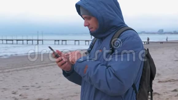 穿着蓝色羽绒服的人在海边的沙滩上打手机留言侧视视频的预览图