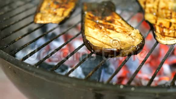 切片的茄子牛排是用烤架或烧烤来煎的然后用厨房的火钳转动一侧的茄子被烧了视频的预览图