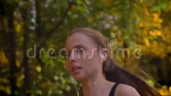 多莉拍摄特写肖像年轻迷人的白种人苗条女孩跑在秋季公园带耳机视频的预览图