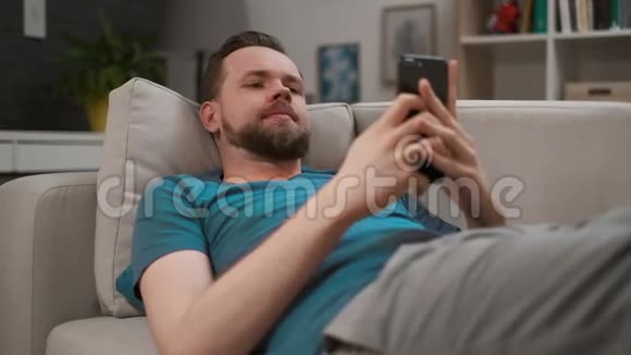 一个英俊的男人在家里在智能手机上打字和发短信的肖像男性使用数字移动设备浏览视频的预览图