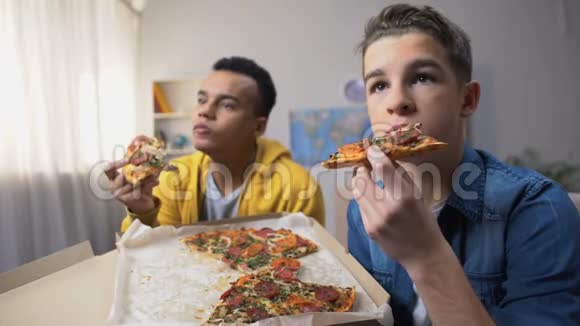 两个多民族的青少年吃披萨看电视节目闲暇时间视频的预览图