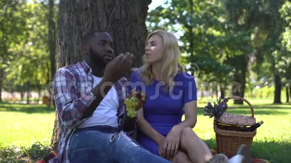 混合种族夫妇在公园里吃葡萄说话在一起视频的预览图