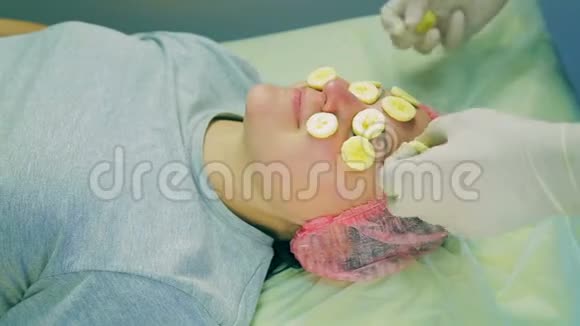 一位戴手套的男性美容师的手从女人的脸上摘下一根香蕉碎片视频的预览图