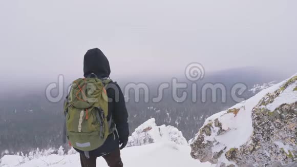 一个背着背包的年轻人站在一座白雪覆盖的山上欣赏着风景视频的预览图