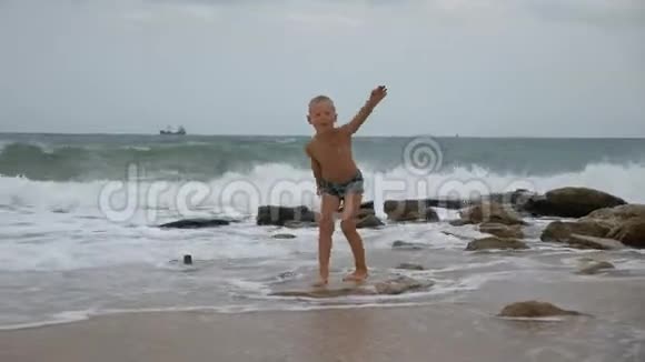 在汹涌的大海上穿着泳裤的男孩站在强壮的石头上试图保持平衡视频的预览图