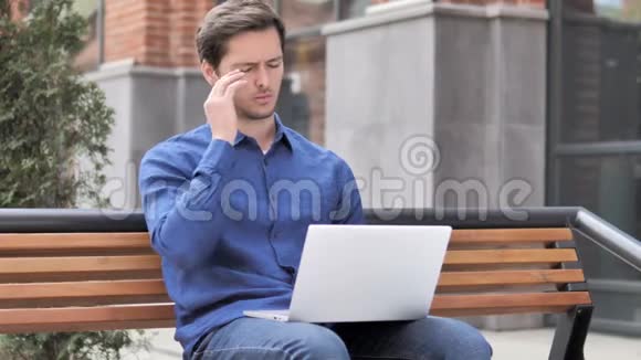 坐在室外头痛的年轻人手提电脑视频的预览图