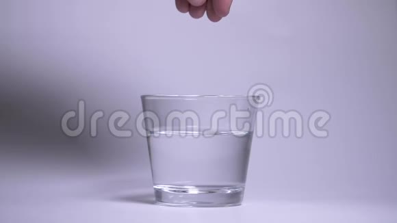 男人的手把两片蓝色泡腾药片扔进一杯水中慢动作药丸在水中溶出气泡视频的预览图