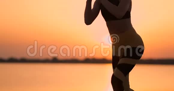 从侧面看年轻女人在户外蹲站在湖边的年轻健身女子蹲着蹲着视频的预览图