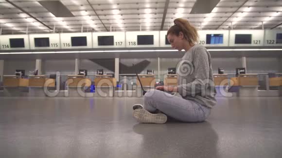 女孩坐在机场地板上的候机楼里在等待航班时用笔记本电脑工作视频的预览图