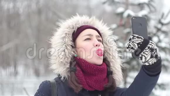 年轻漂亮的女孩在冬天的公园里散步时在她的智能手机上拍照视频的预览图