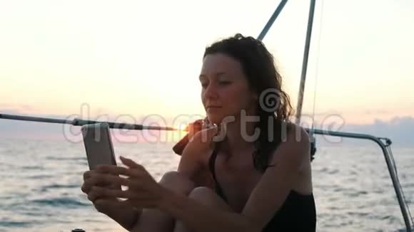 年轻女子驾驶游艇使用智能手机日落时自拍视频的预览图