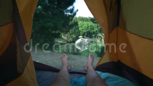 一个年轻人腿躺在帐篷里徒步旅行一天后休息一个人躺在靠近绿色森林的帐篷里视频的预览图