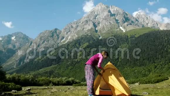 快乐的女游客打开帐篷坐在营地的一座高山的背景下视频的预览图
