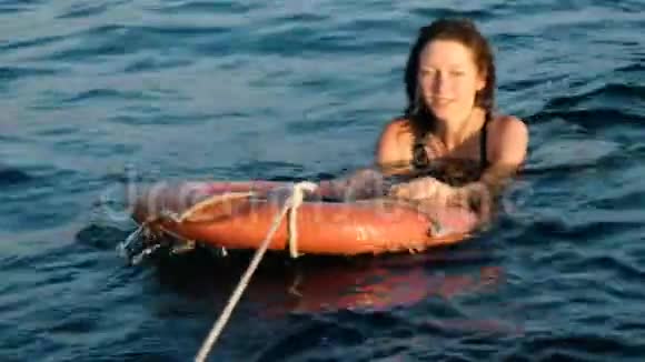 一位年轻的美女穿着泳衣在海上日落时抱着救生圈视频的预览图