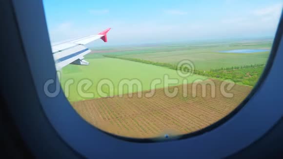 从绿色的农田和蓝天上的飞机窗口鸟瞰视频的预览图