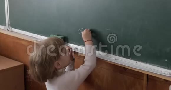 女孩在教室里用粉笔在黑板上画画教育进程视频的预览图