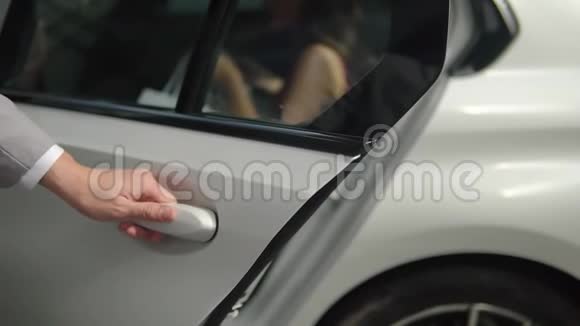 身着灰色制服的司机在夏日里关上了后座上的汽车特写女士的门视频的预览图