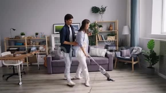 夫妻二人在现代公寓里用吸尘器吸地板跳舞视频的预览图