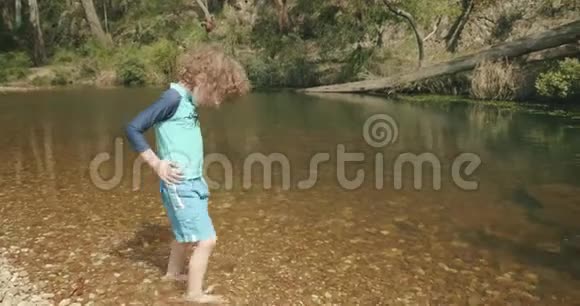 小男孩和小女孩在一条有着清澈水的浅石卵石河里玩耍视频的预览图