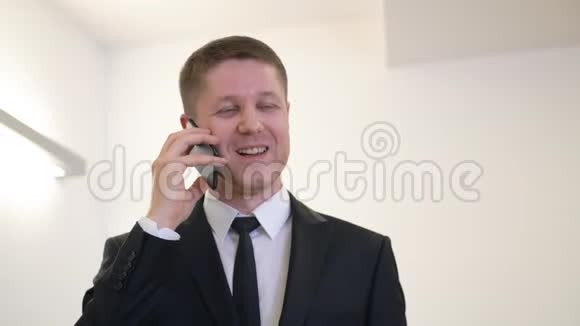 一个开朗的商人在办公室里微笑着用手机说话视频的预览图