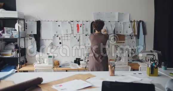 女服装设计师看挂在墙上的服装图纸视频的预览图