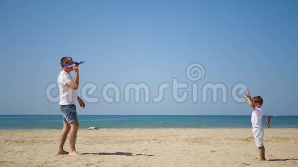 海沙滩上一对幸福的父子正对着对方发射了一架玩具飞机幸福的概念视频的预览图
