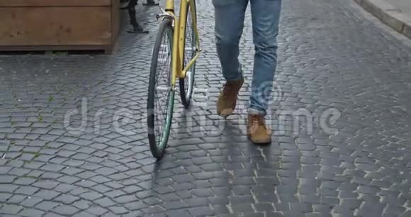 在现代黄薄轮胎自行车附近的旧石洞上行走的牛仔裤和休闲靴的腿特写镜头视频的预览图