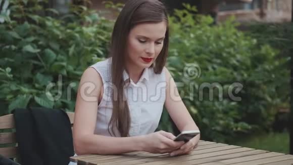 年轻的商务女性坐在夏天的咖啡馆里和智能手机聊天视频的预览图