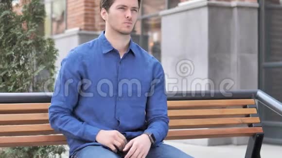 背部疼痛的年轻人坐在户外长椅上视频的预览图