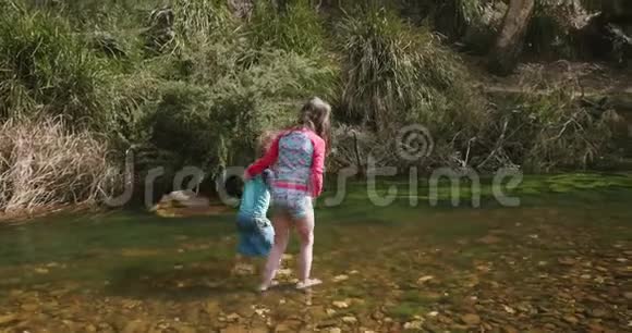一个年轻的女孩在河中的水中膝下行走支撑着一个年轻的男孩视频的预览图