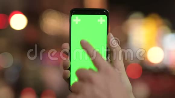 晚上用带绿色屏幕的屏幕的手机在灯光下进行特写视频的预览图
