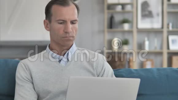 中年男子坐在沙发上用笔记本电脑工作视频的预览图