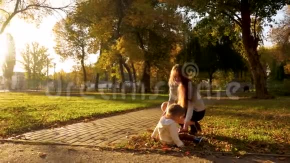 妈妈在秋天公园的草坪上和带着干黄叶子的宝宝玩孩子坐在草地上妈妈从视频的预览图