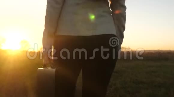商务女性穿着裤子手里拿着公文包在美丽的夕阳下穿过田野背面视图视频的预览图