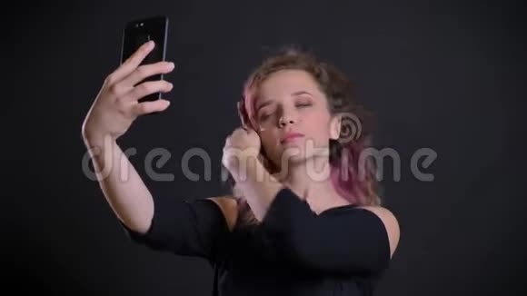 年轻的高加索女孩的肖像粉红色的头发制作自拍照片使用智能手机在黑色背景视频的预览图